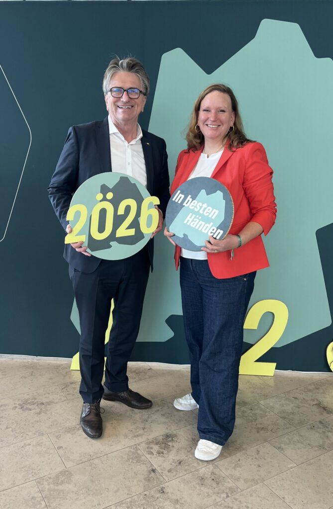 Landtagskandidatin Anna Wiech und Landtagsabgeordneter Manne Lucha posieren vor einer Leinwand.